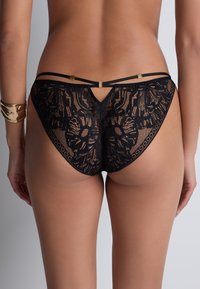 Bikini en dentelle noire avec motif floral, doté de fines bretelles et d'un détail en trou de serrure au dos, agrémenté de accessoires en or.