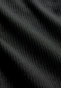 Černá žebrovaná látka s texturovaným povrchem, která má vertikální linie pro zvýraznění hloubky. Hladký a pružný materiál.