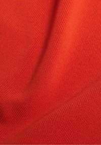 Červená pletená tkanina s jemnou žebrovanou strukturou, která má hladké povrchy a jemné odstínové variace. Žádné viditelné vzory nebo další detaily.