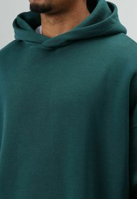 Dunkelgrüner Kapuzenpullover aus weichem Stoff, mit großer Kapuze, weiter Passform und glatter Oberfläche ohne sichtbare Muster oder Verzierungen.