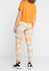 Pomarańczowy krótki t-shirt zestawiony z leginsami w nadruki w pomarańczowe, szare i kremowe faliste wzory, dopełniony czarno-białymi sneakersami.