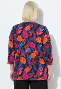 Blumenbluse mit lila Hintergrund und lebhaften orange, pink und blauen Blumen. Dreiviertelärmel und lockere Passform.