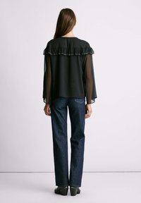 Top negro transparente con cuello con volantes, adornado con piedras, combinado con jeans rectos de color azul oscuro y zapatos de tacón verdes.