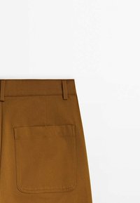 Bruine katoen broek met een platte voorkant, riemlussen en een grote achterzak met een rechthoekige klep. Gladde textuur met strakke lijnen.