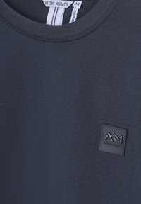 Camiseta de color navy hecha de tela suave con un escote de cuello redondo y un parche texturizado negro con "AM" en la parte inferior derecha.