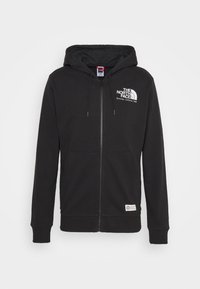 Sweat à capuche zippé noir avec poches avant et logo "The North Face" sur la poitrine gauche et un petit patch près de la taille.