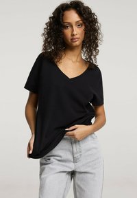 Czarna koszulka z krótkim rękawem i dekoltem w kształcie litery V, wykonana z miękkiego materiału, zestawiona z jasnoszarymi dżinsami z wysokim stanem. Casualowy i luźny krój.