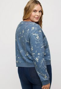 Sudadera de patrón floral azul hecha de una tela suave, con un cuello redondo y puños acanalados. El diseño incluye estampados botánicos en tonos claros.