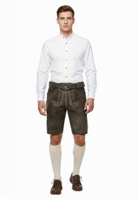 Traditionelt bayersk outfit med en hvid skjorte med plisseringer, mørke shorts med gule accenter og knæhøje cremefarvede sokker.