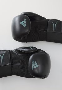 Zwarte bokshandschoenen met textuur van mesh-stof en gewatteerde knokkels. Voorzien van blauwe accenten en het Adidas-logo op de pols en handschoenen.