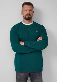 Teal crewneck sweatshirt met lange mouwen, geribbelde boorden en rand. Bevat een klein logo patch op de borst en een witte binnenkraag.