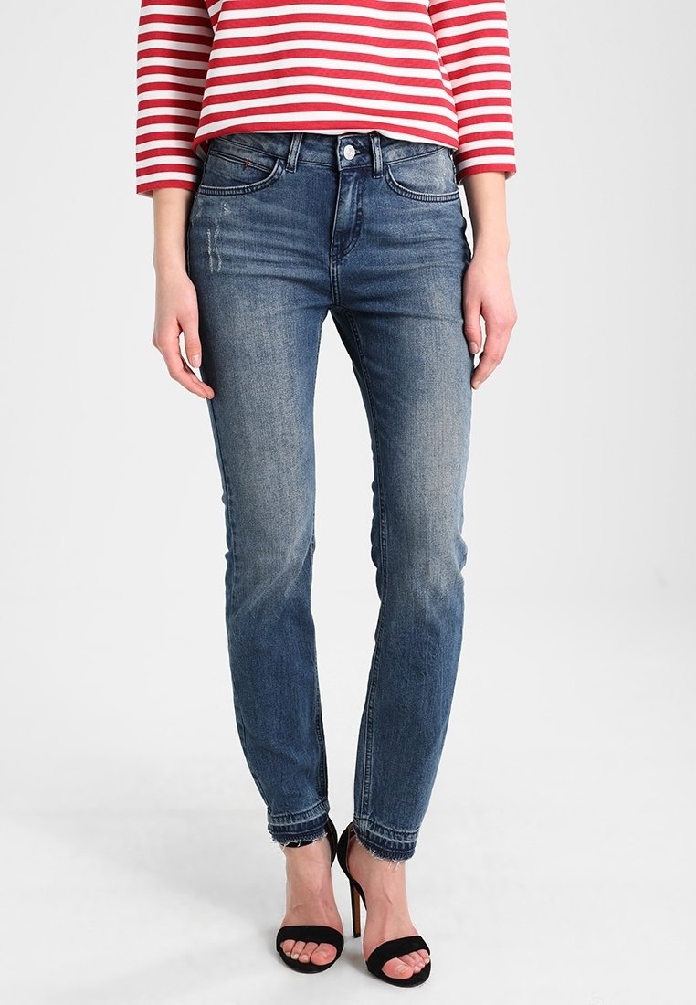 Hubené džíny z tmavě modrého denimového materiálu s mírným vyblednutím, s pěti kapsami a standardním zapínáním na knoflík. Nalezeno s otevřenými černými podpatky.