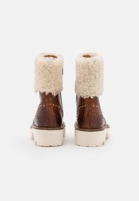 Botas de imitación de cocodrilo marrones con un puño de borreguito blanco y esponjoso, suela blanca resistente y tachuelas decorativas a lo largo de los lados.