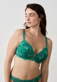 Soutien-gorge en dentelle vert émeraude avec des bords festonnés et des broderies florales. Il est doté de bretelles réglables et d'un décolleté plongeant.