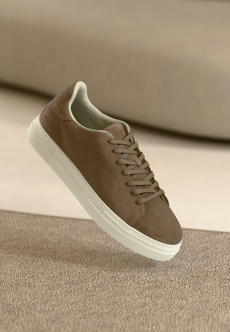 Brune suedesneakers med en glat overflade, snørebåndsdesign og hvid gummisål. Har en afrundet tå og strømlinet form.