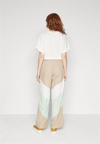 Losse, cropped witte t-shirt met opgerolde mouwen. Beigekleurige, witte en mintgroene zigzag-patroon wijde broek. Gele sneakers.