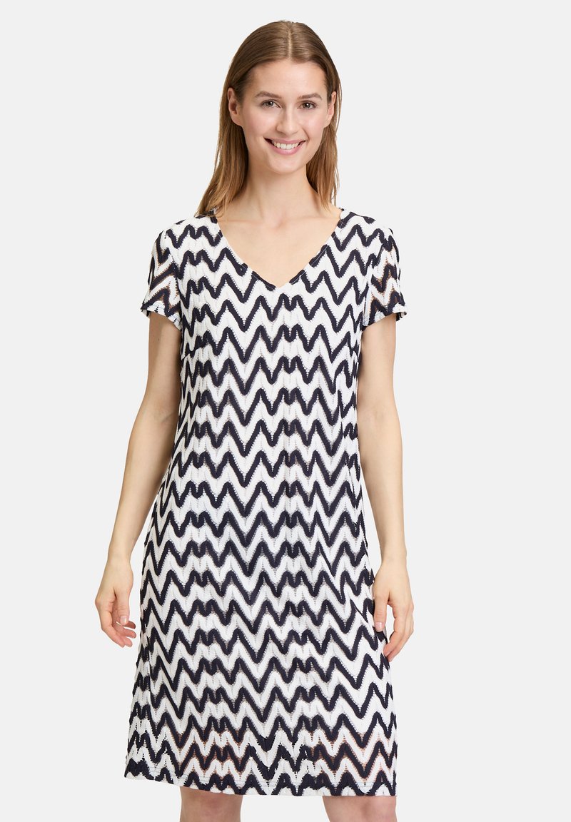Kurzes Kleid mit einem navyblauen und weißen Zickzackmuster, V-Ausschnitt und lässiger Passform. Hergestellt aus leichtem Stoff mit texturierter Oberfläche.