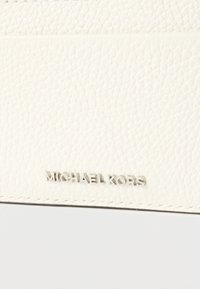 Producto de cuero blanco texturizado con costuras visibles y logotipo "MICHAEL KORS" en relieve en plata metálica en la sección inferior.