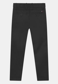 Czarne spodnie wykonane z gładkiej tkaniny, o prostym kroju nogawki, z paskiem na gumce i pętelkami na pasek, z dwiema tylnymi kieszeniami zapinanymi na guziki.