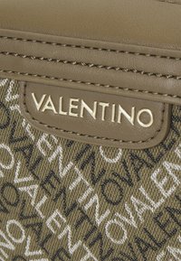 Borsa in tessuto marrone con motivo a logo "Valentino" ripetuto in bianco e nero, arricchita da una placca con logo in tonalità oro e design strutturato.