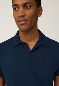Dunkelblaues Poloshirt mit kurzen Ärmeln und einem entspannten Kragen. Verfügt über eine kleine Tasche mit einem dezenten gestickten Logo. Weicher Stoff.