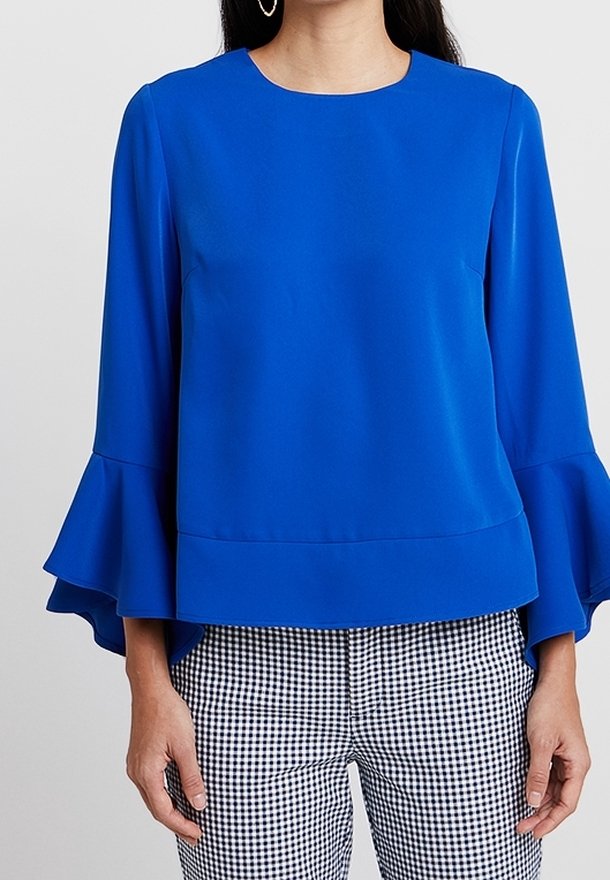 Królestwony niebieski top z długim rękawem, okrągłym dekoltem i rozszerzanymi mankietami, zestawiony z czarno-białymi spodniami w kratkę gingham. Gładka faktura materiału.