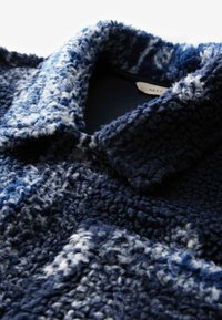 Marineblauwe en witte fleecejack met een gepatroond, textuur rijk en luxueus oppervlak, brede kraag en knoopsluiting, die een gezellige en warme uitstraling heeft.