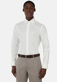 Camicia bianca a maniche lunghe con colletto a punta, abbinata a pantaloni a quadri grigio chiaro e una cintura marrone. Tessuto dalla texture liscia.