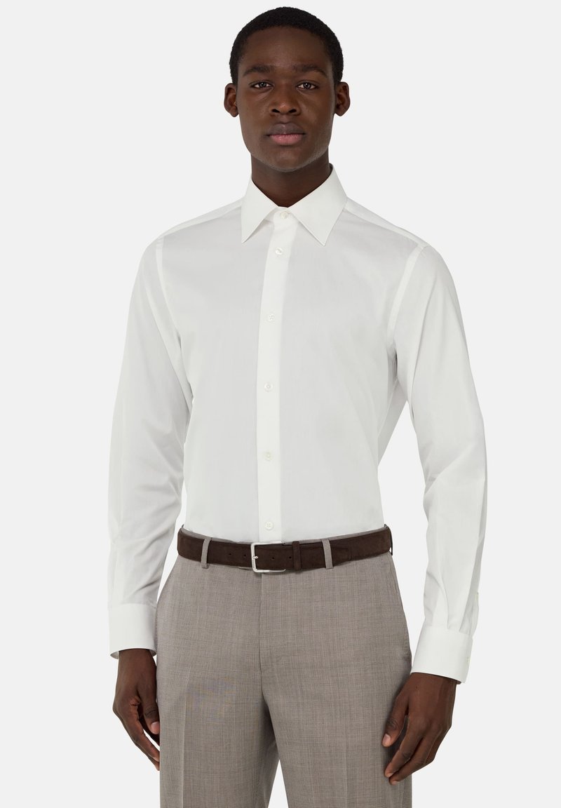 Camicia bianca a maniche lunghe con colletto a punta, abbinata a pantaloni a quadri grigio chiaro e una cintura marrone. Tessuto dalla texture liscia.