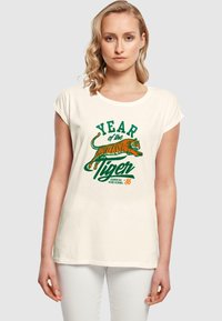 Cremefarvet bomulds t-shirt med rullede korte ærmer, der har et farverigt tiger-tryk og teksten "År for tigeren" i grøn og orange.