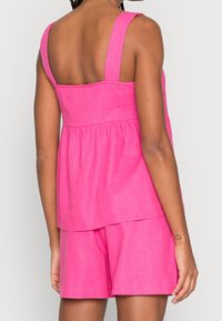 Haut sans manches rose vif avec un col carré et une taille froncée, assorti à un short, fabriqué dans un tissu léger texturé.