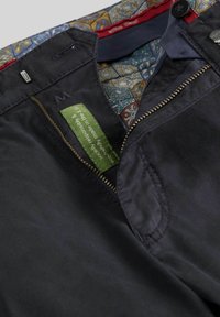 Pantalons en tissu bleu marine avec doublure à motif contrasté, fermeture éclair et étiquette verte indiquant une fabrication responsable dans l'UE.