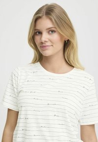 Hvid bomulds T-shirt med rund hals, prydet med et mønster af bynavne i sort kursiv tekst på vandrette linjer. Korte ærmer, afslappet pasform.