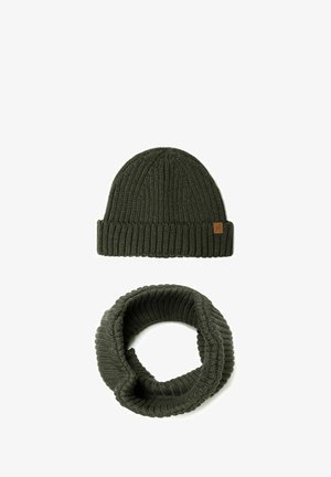 Bonnet tricoté vert foncé avec une texture côtelée et une étiquette en cuir, associé à une écharpe en boucle côtelée de couleur vert foncé.