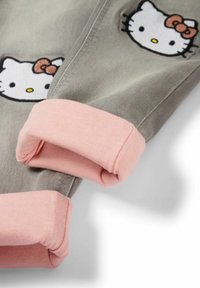 Pantalon gris avec revers roses repliés et visages blancs Hello Kitty brodés avec des nœuds rouges près des revers.