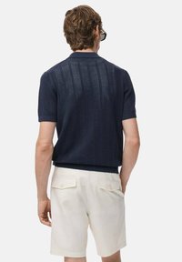 Camisa polo de punto de manga corta en color marino con un patrón texturizado y un cuello acanalado, combinado con pantalones cortos color crema con bolsillos de solapa.