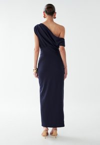 Vestido azul marino de un solo hombro con tela drapeada, cintura ceñida y largo hasta el suelo, con una textura suave y un brillo sutil.