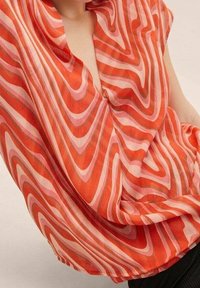 Blusa arancione trasparente con vortici rosa, scollatura a V e maniche corte, caratterizzata da una vestibilità comoda e una texture fluida.