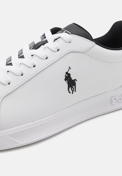 White sneaker with a smooth synthetic upper, black leather accents, flat white laces, and a black embroidered logo of a polo player.
