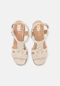 Sandalias beige con correas de tela trenzada y una plantilla de textura suave. Presenta una correa en el tobillo con un acento de hebilla en tono dorado.