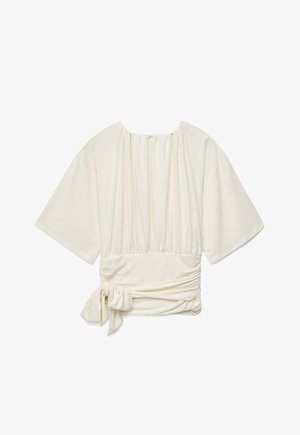 Blusa color marfil con mangas anchas hasta el codo, escote fruncido y cintura fruncida con lazo en el lado izquierdo.