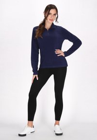 Marine fleece pullover med halvdækning, parret med sorte leggings og hvide sneakers. Glat tekstur, afslappet design.