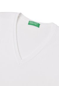Biała koszulka z bawełny z dekoltem w serek, z prążkowaną fakturą wokół linii szyi. Zielona metka z napisem „UNITED COLORS OF BENETTON.”