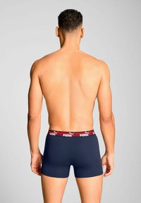 Navy blue boxer shorts made of soft fabric, featuring a red and white branded waistband. The design is fitted with a smooth texture.