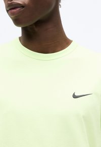 Κοντινό πλάνο ενός ατόμου που φοράει ανοιχτοπράσινη μπλούζα Nike με μαύρο λογότυπο Nike στην περιοχή του στήθους.