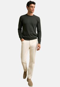 Sötétzöld pulóver, könnyű kötött anyag, kerek nyakkivágás, hosszú ujjak. Bézs nadrág, slim-fit, sima textúra, barna slip-on cipővel párosítva.