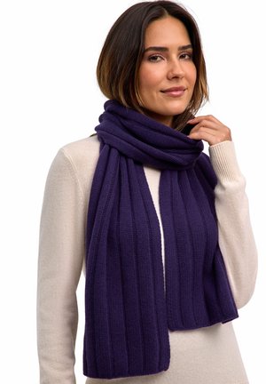 Paarse geribbelde sjaal van gebreide stof, om de nek gedrapeerd, in contrast met een licht crèmekleurige trui. De sjaal heeft een zachte textuur.