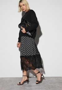 Black oversized sweatshirt paired with a polka dot skirt featuring a lace hem. Black strappy heels complete the outfit. Model holds a black bag.