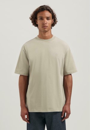 T-shirt beige clair à manches courtes avec un col rond et un subtil logo brodé sur la poitrine. Fabriqué en coton doux et respirant.