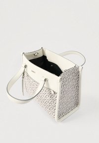 Baltos ir smėlio spalvos rankinė su DKNY logotipo raštu, dvi rankenos, priekinė kišenė su užtrauktuku ir atviras viršus, rodantis juodą vidinę pamušalą.